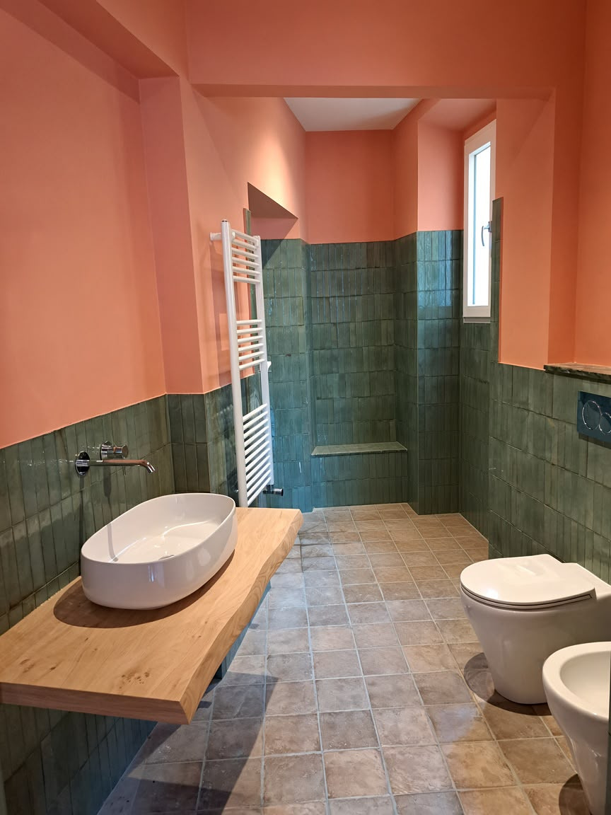 Bagno ristrutturato con piastrelle verdi, lavabo in legno e sanitari sospesi